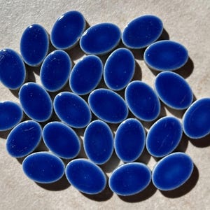 Puede incluir: Una colección de 20 azulejos de cerámica ovalados de color azul oscuro. Los azulejos tienen un borde blanco y una superficie ligeramente texturizada.