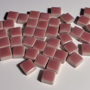 May include: A pile of small, square, dusty rose colored ceramic tiles.
