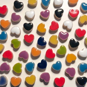 Peut inclure: Une collection de petits objets en forme de cœur dans une variété de couleurs brillantes, notamment rouge, orange, jaune, vert, bleu, violet, blanc et noir. Chaque cœur présente une surface lisse et réfléchissante ainsi qu'une forme arrondie.