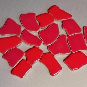 Peut inclure: Un ensemble de carreaux de céramique rouges brillants de forme irrégulière. Les carreaux varient légèrement en teinte, allant d'un rouge profond à un rouge plus vif. Ils sont dispersés sur un fond gris neutre.