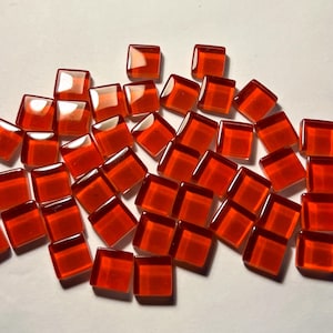 Peut inclure: Un ensemble de petits carreaux de verre rouges translucides et carrés. Chaque carreau a un dessus légèrement arrondi et un bord rouge plus foncé. Ils sont dispersés sur une surface blanche, créant un aspect vibrant et réfléchissant. Idéal pour les projets de mosaïque.