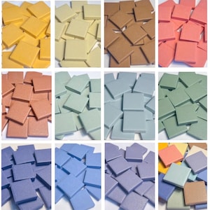 May include: A selection of square tiles in a variety of colours, including yellow, beige, brown, coral, light blue, green, and purple. The tiles are arranged in a grid, showcasing the range of hues available for mosaic or craft projects.