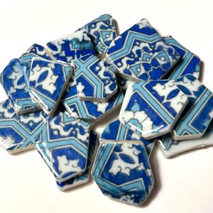 May include: A collection of broken ceramic tiles with intricate blue and white patterns. The tiles are various shapes and sizes, with a glossy finish. The design features geometric shapes and floral motifs, creating a decorative mosaic effect.