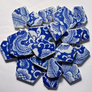 May include: A collection of blue and white ceramic shards with floral and leaf patterns. The pieces are irregularly shaped and arranged in a scattered pile, showcasing a classic, decorative design.