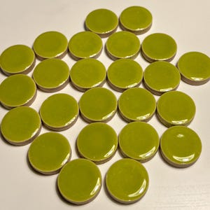 May include: A collection of 20 round, green ceramic tiles. The tiles are approximately 1 inch in diameter and have a glossy finish.