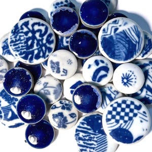 Può includere: Una collezione di piccole piastrelle rotonde in ceramica nei toni del bianco e del blu intenso. Le piastrelle presentano vari motivi, tra cui disegni floreali, forme geometriche e motivi astratti. Alcune piastrelle sono blu tinta unita, altre hanno una base bianca con dettagli blu.