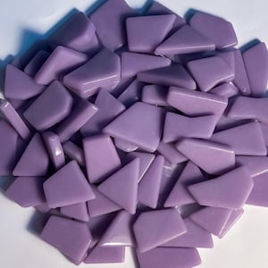 May include: A pile of lavender-colored, irregularly shaped glass mosaic tiles. The tiles have a glossy finish and vary in size and shape, including triangles and trapezoids. These tiles are suitable for various craft projects.