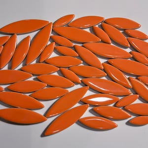 Puede incluir: Una colección de azulejos de cerámica naranja en forma de hoja. Los azulejos son brillantes y tienen un acabado liso.