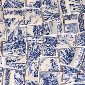 Pode incluir: Uma coleção de peças de cerâmica quebradas com ilustrações azuis e brancas. Os fragmentos apresentam cenas e textos relacionados a Wyoming, incluindo Powder River, o Parque Nacional de Yellowstone e Devils Tower. As peças estão dispostas sobre uma superfície branca.