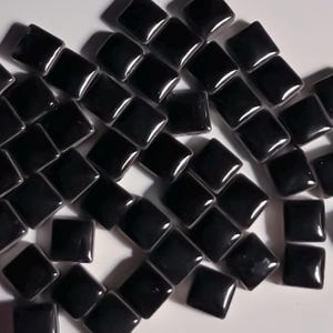 Könnte beinhalten: Eine Sammlung schwarzer quadratischer Mosaikfliesen. Die Fliesen sind glänzend und haben eine glatte Oberfläche.