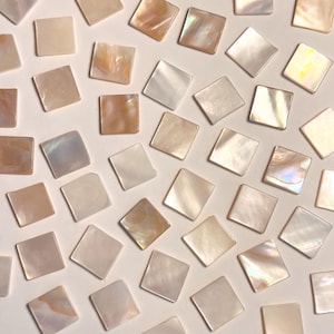 Op de afbeelding: Verspreide vierkante mozaïektegels in tinten wit, crème en perzik. De tegels hebben een parelmoerglans, die licht reflecteert. Ideaal voor knutselprojecten, deze tegels bieden een subtiele, elegante esthetiek.