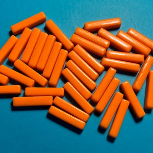 Può includere: Un gruppo di bastoncini di plastica arancioni disposti in uno schema casuale su uno sfondo blu. I bastoncini sono tutti della stessa dimensione e forma, e sono tutti fatti di una plastica liscia e lucida.
