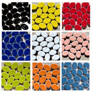 May include: A collection of nine separate groups of small, smooth, oval-shaped ceramic tiles in various solid colors including black, yellow, red, dark blue, white, light pink, lime green, orange, and light blue, arranged in a grid pattern.