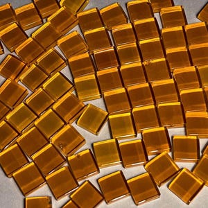 May include: A large quantity of small, square, amber-colored glass tiles. The tiles are scattered on a white surface.
