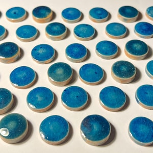 May include: A collection of small, round, ceramic tiles. Each tile features a glossy, turquoise blue glaze with a crackle effect. The edges of the tiles are a light tan color. The tiles are arranged in a grid pattern.
