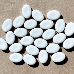 Puede incluir: Una colección de azulejos ovalados de cerámica blanca. Los azulejos son lisos y brillantes, con una ligera variación en tamaño y forma.