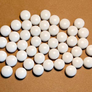 Pode incluir: Uma coleção de azulejos de vidro redondos brancos. Os azulejos são lisos e brilhantes.