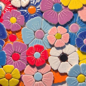 Puede incluir: Un mosaico de flores de cerámica coloridas en tonos de rosa, azul, amarillo, rojo y blanco. Cada flor tiene un centro contrastante, creando un patrón floral vibrante y texturizado. Adecuado para la decoración del hogar.