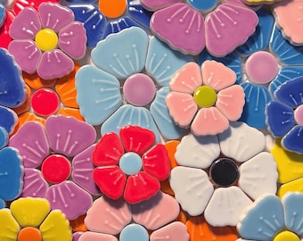 Op de afbeelding: Een mozaïek van kleurrijke keramische bloemen in verschillende tinten roze, blauw, geel, rood en wit. Elke bloem heeft een contrasterend centrum, waardoor een levendig en gestructureerd bloemenpatroon ontstaat. Geschikt voor interieurdecoratie.