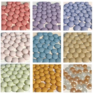 May include: Nine squares of colourful, round sweets in various shades. The colours include pink, purple, blue, white, light blue, beige, green, orange, and a mix of white and gold. The sweets are evenly spaced.