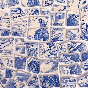 Pode incluir: Uma coleção de peças de cerâmica quebradas com ilustrações azuis e brancas. Os fragmentos apresentam cenas de paisagens, fragmentos de texto e imagens de pessoas e animais. As peças estão dispostas sobre uma superfície branca.