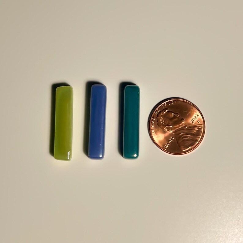 May include: Three glass tiles in different colors: a light green tile, a blue tile, and a teal tile. The tiles are all rectangular and about the size of a US penny.