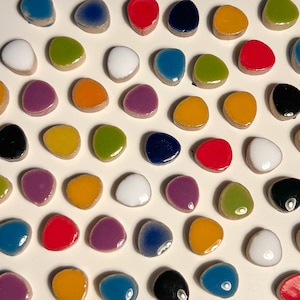 May include: Assortment of colorful ceramic tiles in various shapes and sizes. The tiles are arranged in a pattern on a white background.