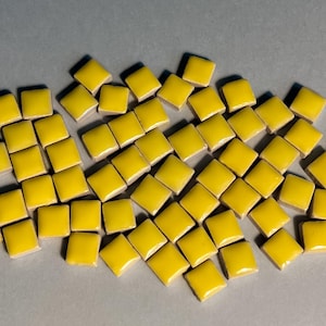 May include: A large pile of small, square, yellow ceramic tiles. The tiles are arranged in a random pattern.