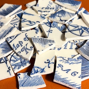 Puede incluir: Un montón de azulejos de cerámica blanca rotos con diseños de brújula azules y blancos y las palabras "Map of K" y "PAG" impresas en ellos.