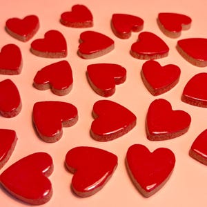 May include: A collection of red heart-shaped tiles arranged in a circular pattern on a light pink background.