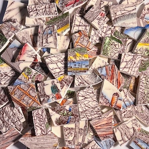 Peut inclure: Un ensemble de fragments de céramique cassés, chacun orné d'illustrations de paysages et d'architecture. Les morceaux présentent un fond crème avec des dessins au trait marron et des touches de couleur, créant un effet mosaïque. Les pièces varient en taille et en forme.