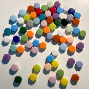 May include: A collection of colourful hexagonal tiles in various shades of blue, green, red, orange, yellow, purple, and white. The tiles are arranged in a loose, organic pattern, creating a visually appealing display.