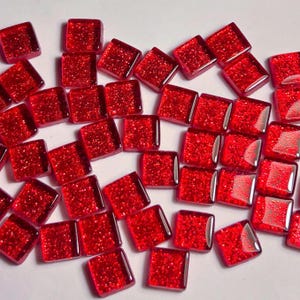 Peut inclure: Un ensemble de petits carreaux de verre rouges carrés avec une surface texturée et scintillante. Les carreaux sont dispersés sur une surface blanche, mettant en valeur leur couleur vibrante et leur qualité réfléchissante. Idéal pour les projets d'art de mosaïque.