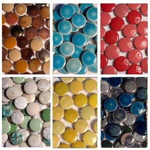 May include: A collection of circular ceramic tiles arranged in six distinct colour groups including brown, turquoise, red, white and green, yellow, and dark blue with speckled patterns. Each tile features a smooth, glossy finish and round shape.