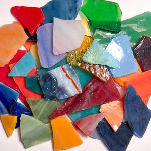 May include: A collection of irregularly shaped, colorful glass pieces. The assortment includes shades of red, blue, green, orange, and yellow. The glass appears to be translucent, with some pieces showing internal patterns. Ideal for mosaic art or stained glass projects.