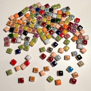 May include: A large assortment of colourful ceramic tiles in various shades of red, orange, yellow, green, blue, purple, and brown. The tiles are square shaped and have a glossy finish.