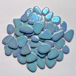 May include: A collection of iridescent, light blue, pebble-shaped decorative stones. The stones have a smooth, glossy surface and vary in size and shape. The color shifts with the light, creating a shimmering effect. Ideal for crafts, mosaics, or home decor.