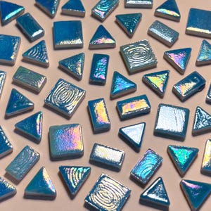 May include: Assortment of iridescent blue glass mosaic tiles in various shapes, including squares, triangles, and diamonds. The tiles have a subtle shimmer and a textured surface.