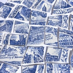 May include: A collection of broken ceramic tiles with blue and white illustrations of buildings and landmarks. The tiles feature architectural sketches and text, including "Nebraska State Capitol" and "Memorial Stadium University of Nebraska."
