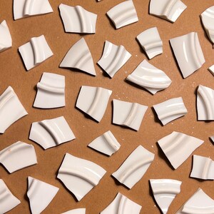 Puede incluir: Una colección de azulejos de cerámica blanca con un diseño curvo. Los azulejos están dispuestos sobre una superficie marrón.