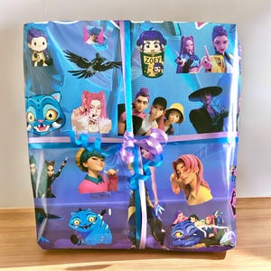 May include: A wrapped gift, predominantly blue and purple, decorated with cartoon character stickers. The wrapping paper displays illustrations of animated figures and a blue cat. A light blue and purple ribbon with a bow adorns the package.