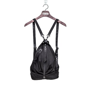 May include: A black backpack with adjustable straps hanging from a wooden hanger. The backpack has a unique, gathered design and a zipper closure.