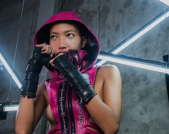 May include: A woman wearing a pink hooded top with a black zipper and barbed wire detail. She is wearing black leather gloves and has a serious expression on her face.