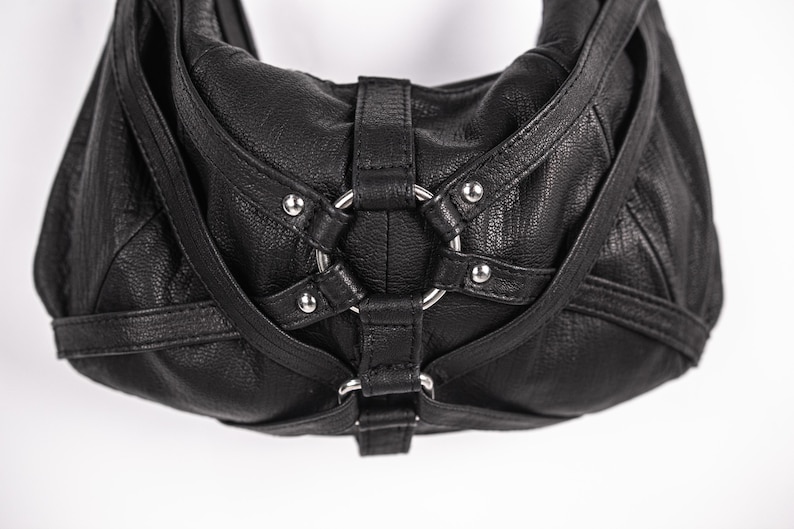 K&ouml;nnte beinhalten: Schwarze Hobo-Tasche aus Leder mit silberfarbenen Beschl&auml;gen. Die Tasche hat eine strukturierte Oberfl&auml;che, ein gro&szlig;es Metallringdetail und verstellbare Riemen. Ein stilvolles Accessoire f&uuml;r den Alltag.