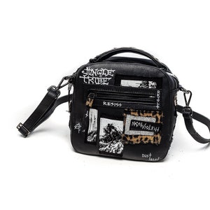 May include: Black crossbody bag with a square shape and a top handle. The bag has a variety of patches and text including "JUNGLE TRIBE", "RESIST", "NON-VIOLENT", and "DUST DREAM".