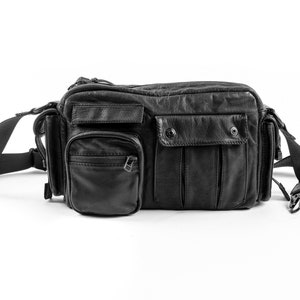 May include: A black leather crossbody bag with multiple pockets and a zipper closure. The bag has a long adjustable strap.