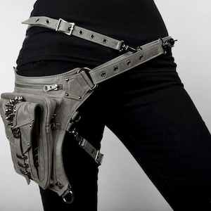 May include: A gray leather thigh holster with a zippered pocket and metal accents. The holster is attached to a wide gray leather belt with metal buckles.