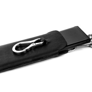 Pu&ograve; includere: Una custodia per telefono in pelle nera con un fermaglio argentato e una catena argentata.