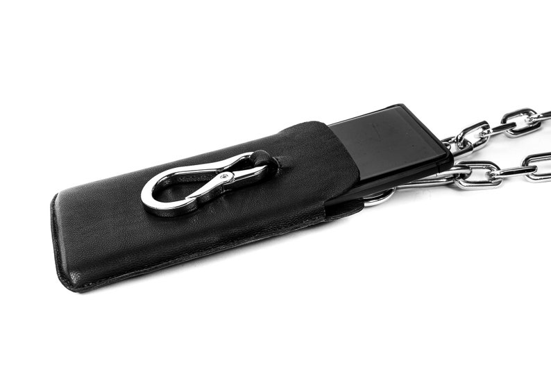 Pu&ograve; includere: Una custodia per telefono in pelle nera con un fermaglio argentato e una catena argentata.