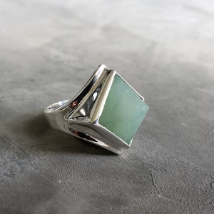 Peut inclure: Une bague en argent avec une pierre précieuse carrée verte sertie dans un sertissage à bélière.